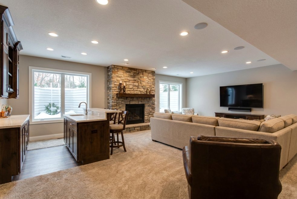 Finished basement living room with stone fireplace, sectional sofa, kitchen island, and recessed lighting